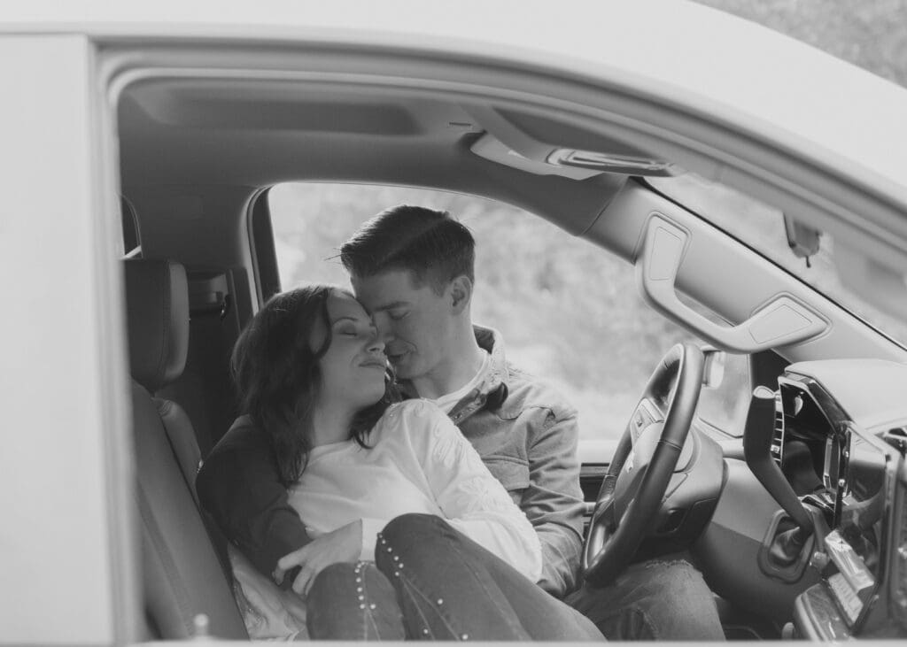 intimate black and white photo of couple snuggled up in a pickup truck 