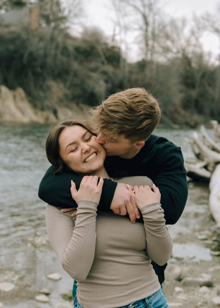 boyfriend kissing girlfriend on the cheek by the river 