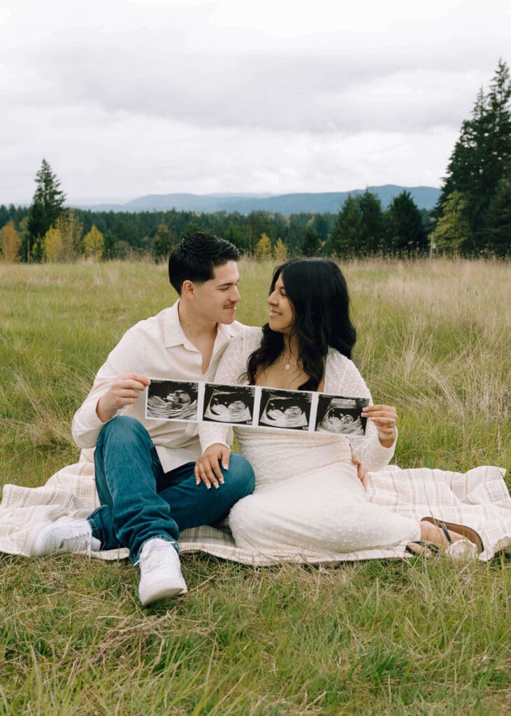 couple sitting on a blanket with ultrasound photos looking at each other in Washington