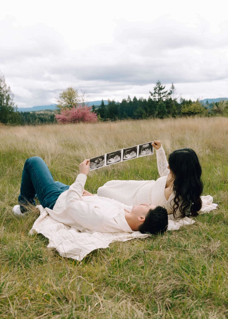 couple wearing white and laying on a blanket looking at ultrasound at Tanwax country chapel
