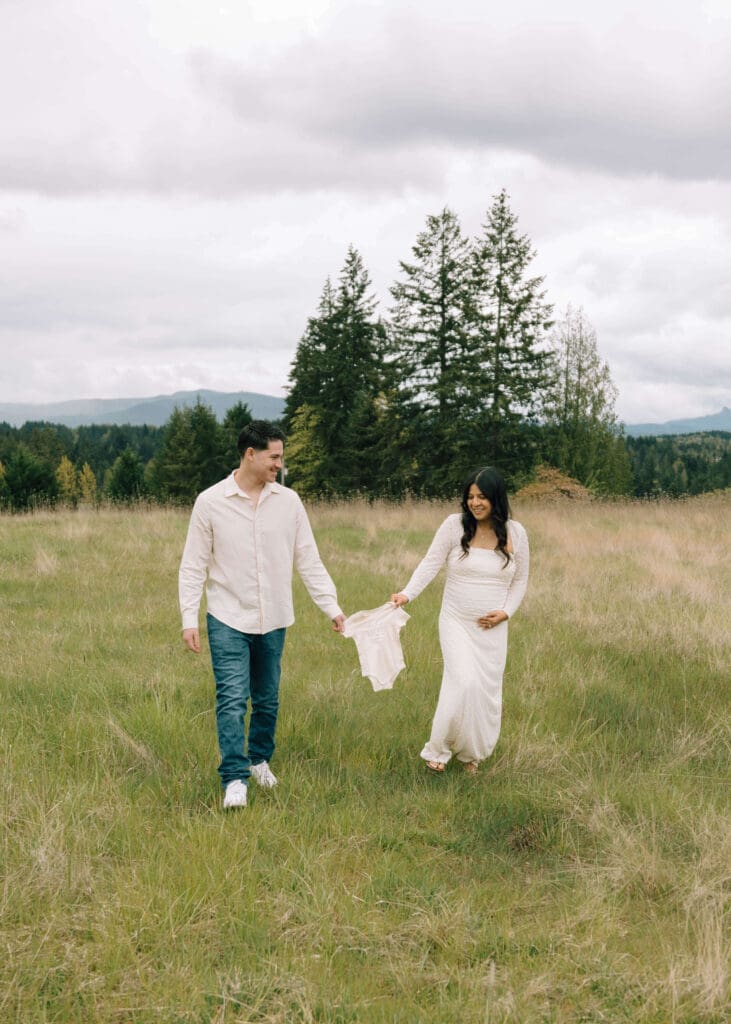 couple walking at tanwax country chapel holding a cream onesie between them wearing white