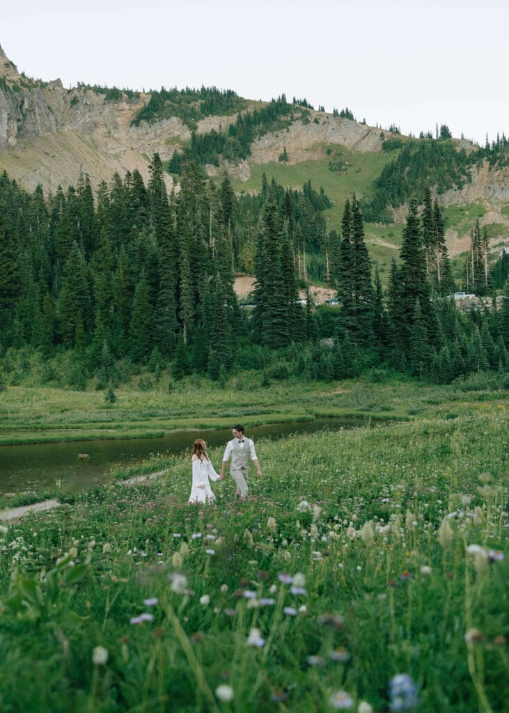 bride and groom hand in hand in a meadow of wildflowers at Tipsoo Lake
