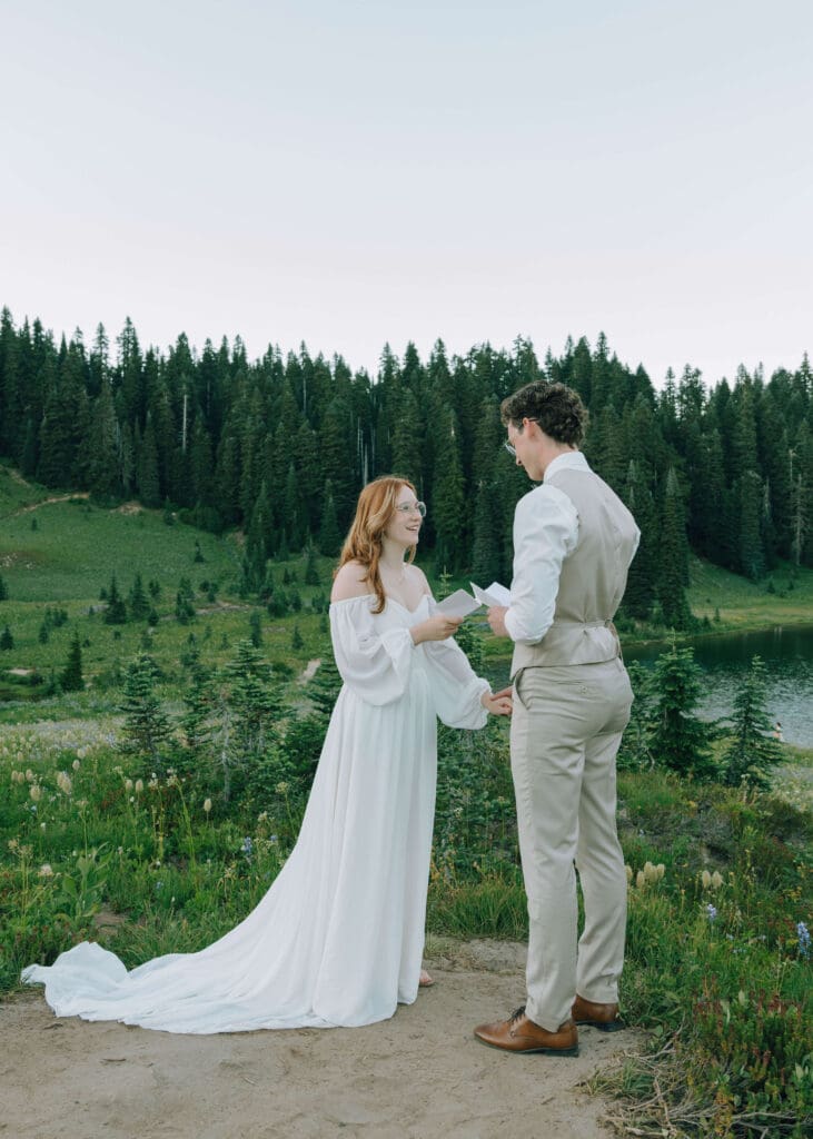 bride and groom holding hands and exchanging vows overlooking Lake Tipsoo with wildflowers 