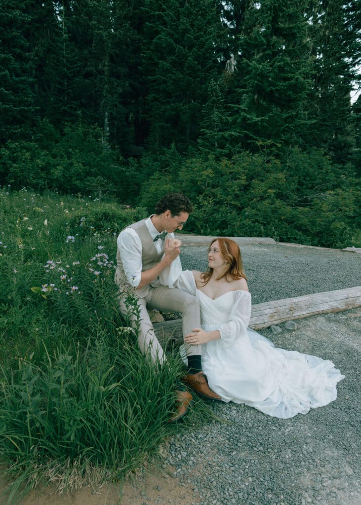 bride and groom sitting in Mt. Rainier before getting married with groom kissing his bride's hand 