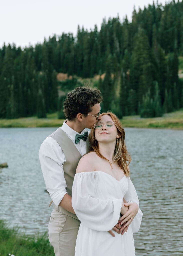 groom kissing his bride's head in front of Lake Tipsoo at Mt Rainier national park elopement