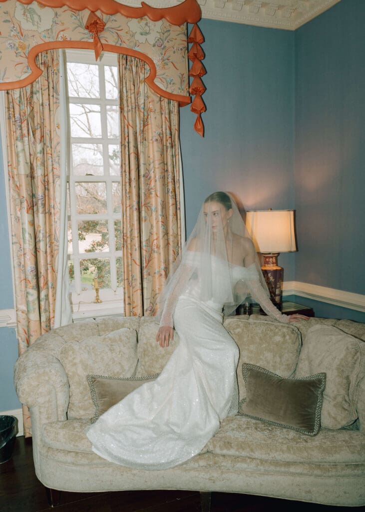 bride sitting on a couch with veil over her face with window behind her at estate at river run 