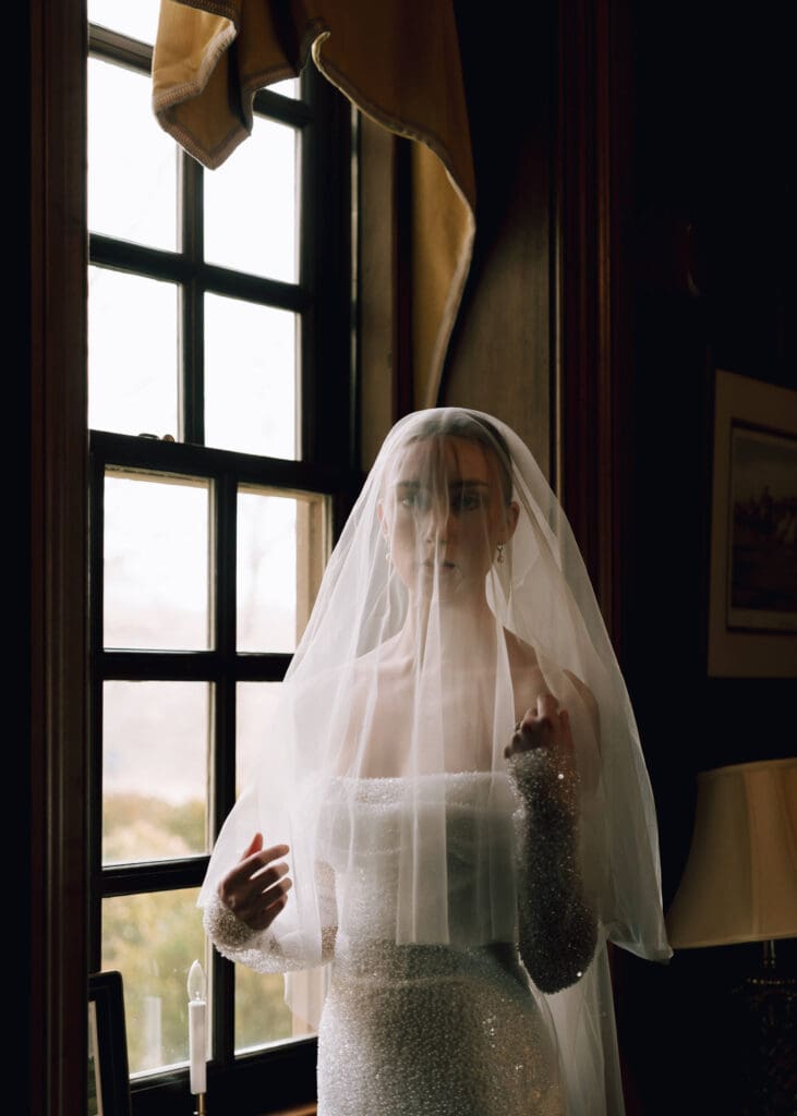 bride with veil over her face in front of window at wedding venue