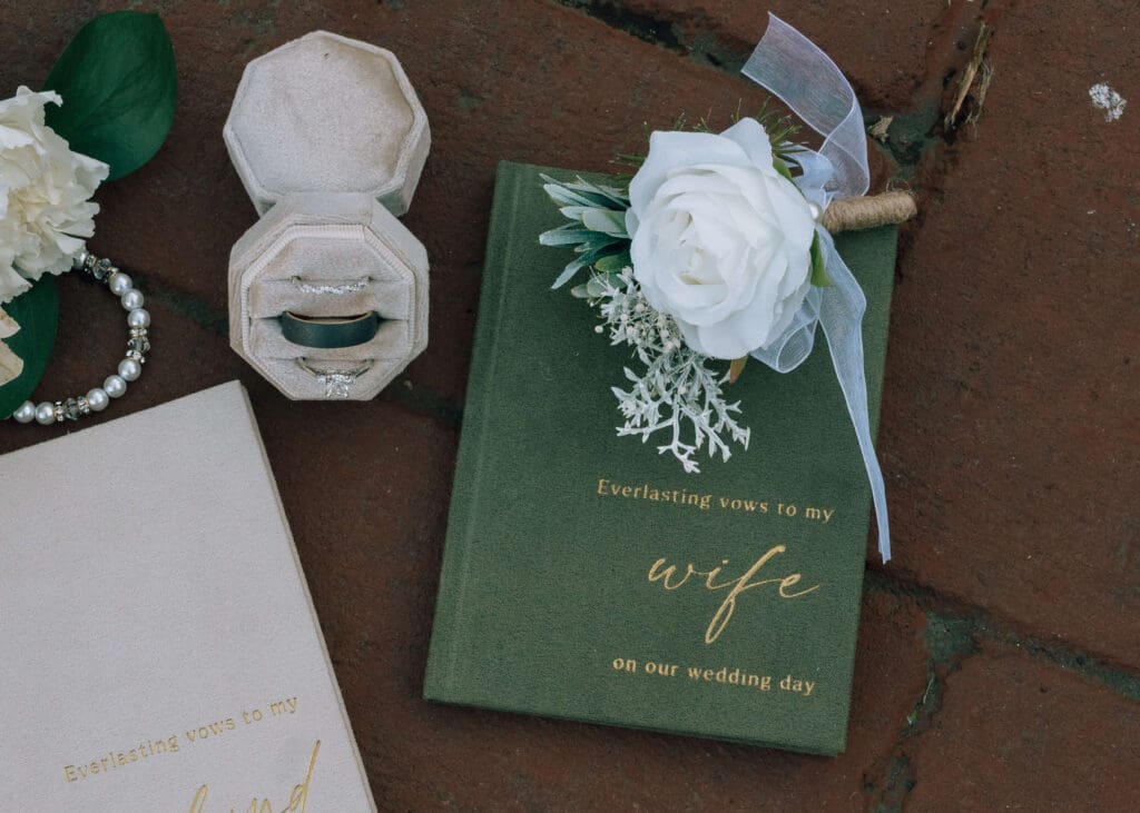 green vow book, white rose boutonniere, white box with 3 rings and cream vow book 