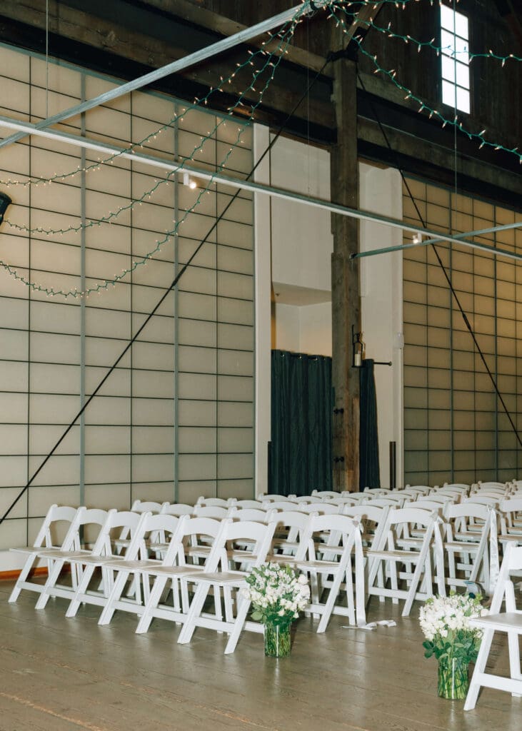 white chairs for indoor ceremony with vases of white flowers set up for Issaquah barn wedding 
