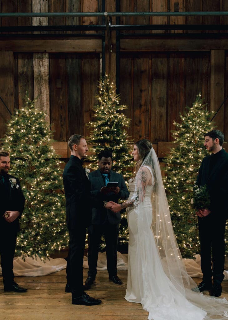 bride and groom holding hands at ceremony in front of christmas trees at Pickering Barn 