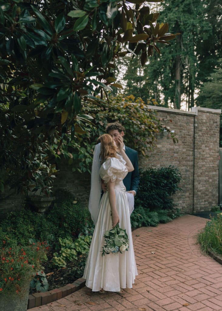 couple touching noses and almost kissing in the garden wedding venue while bride holds blue bouquet