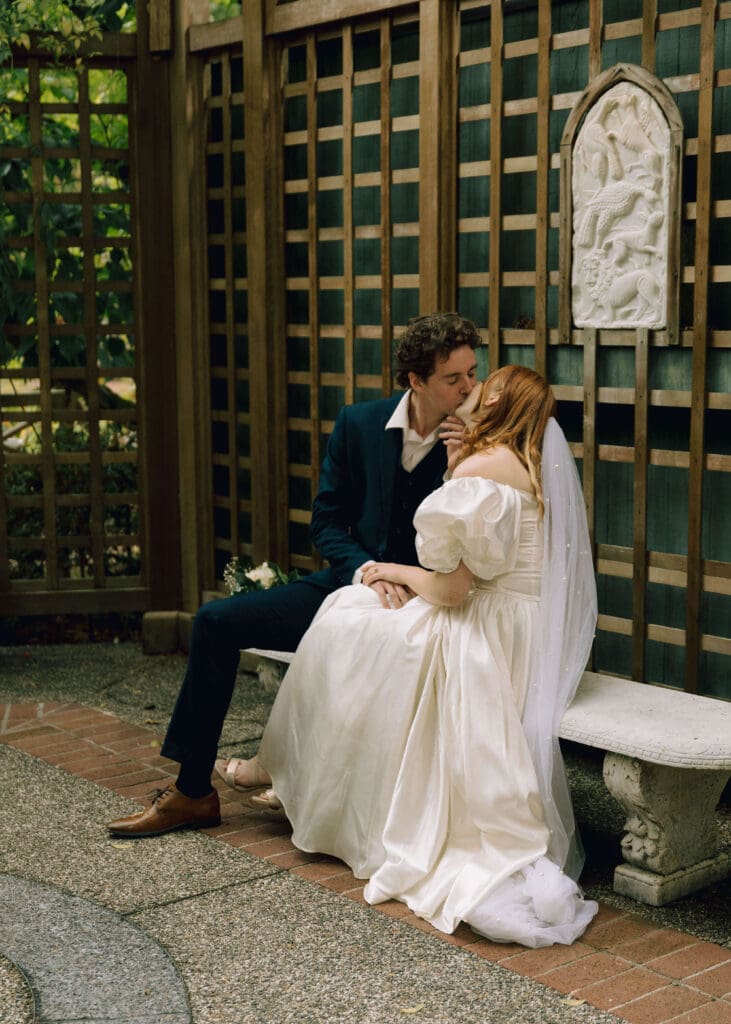 couple sitting on a bench in a garden kissing at Lakewold gardens 