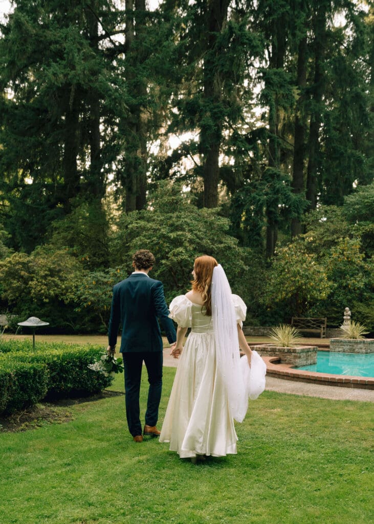 bride and groom walking in a green garden with a decorative pool at Lakewold gardens wedding venue 