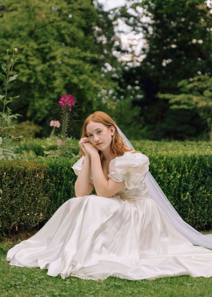 bride squatting in the garden with her hands folded at Lakewold gardens 