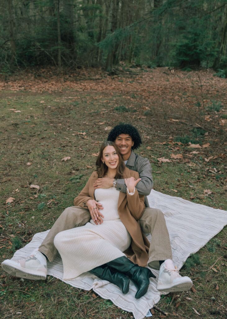 couple sitting on a blanket with man holding the woman from behind 