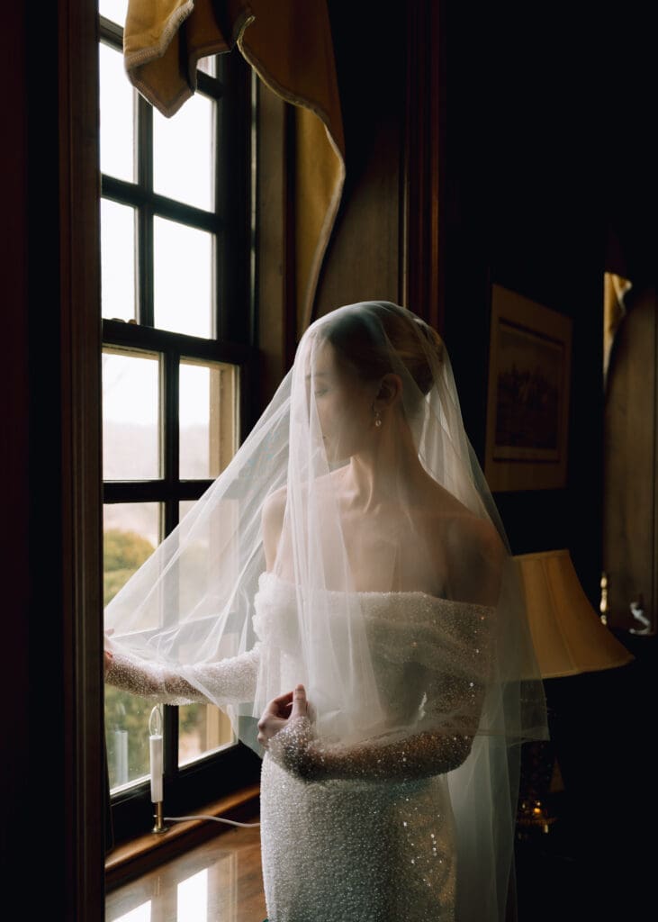 bride in front of window at wedding venue playing with her veil - reasons to get bridal portraits done