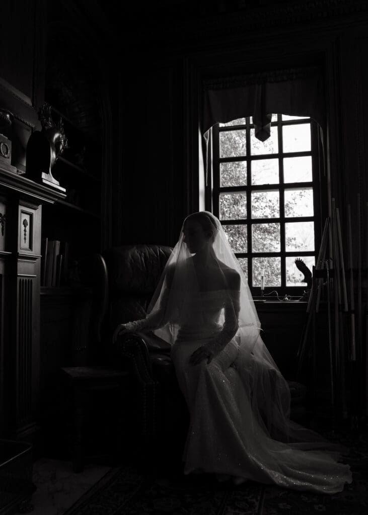 reasons to get bridal portraits done - bride under veil in front of a window sitting in a chair 