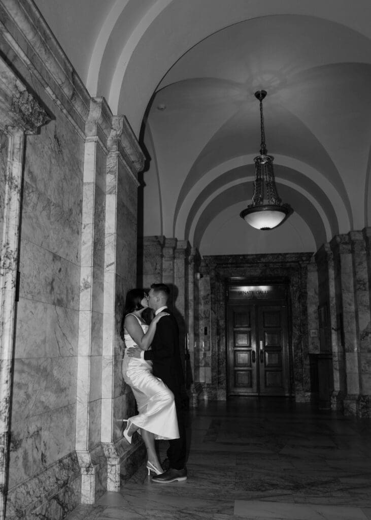 bride leaning against marble wall and kissin her groom in Olympia