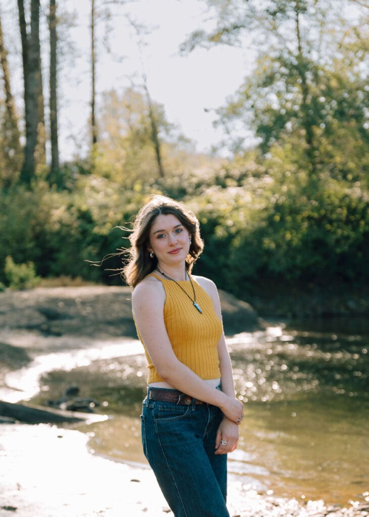 senior girl holding her wrist with the sun behind her 