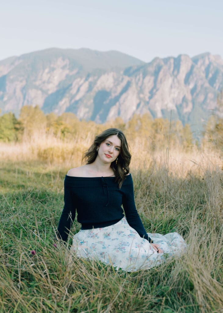 senior girl at Steilacoom High School sitting down in field in front of mountain 