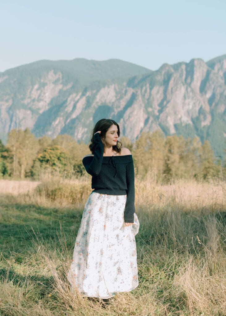 senior girl in a skirt posing in a field with a mountain in the background 