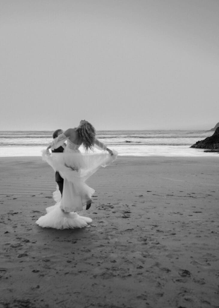 groom twirling his bride around on the beach at sunset 