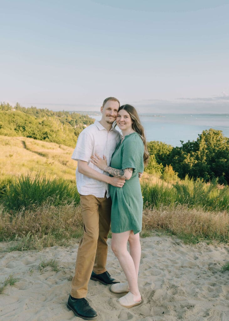 couple smiling and posing for photo at park with puget sound in the background at Seattle engagement photo locations