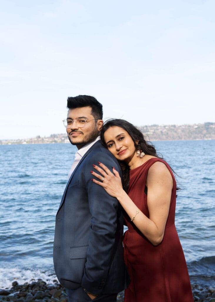 woman in red dress leaning on her fiance's shoulder with the ocean in the background at Seattle engagement photo locations