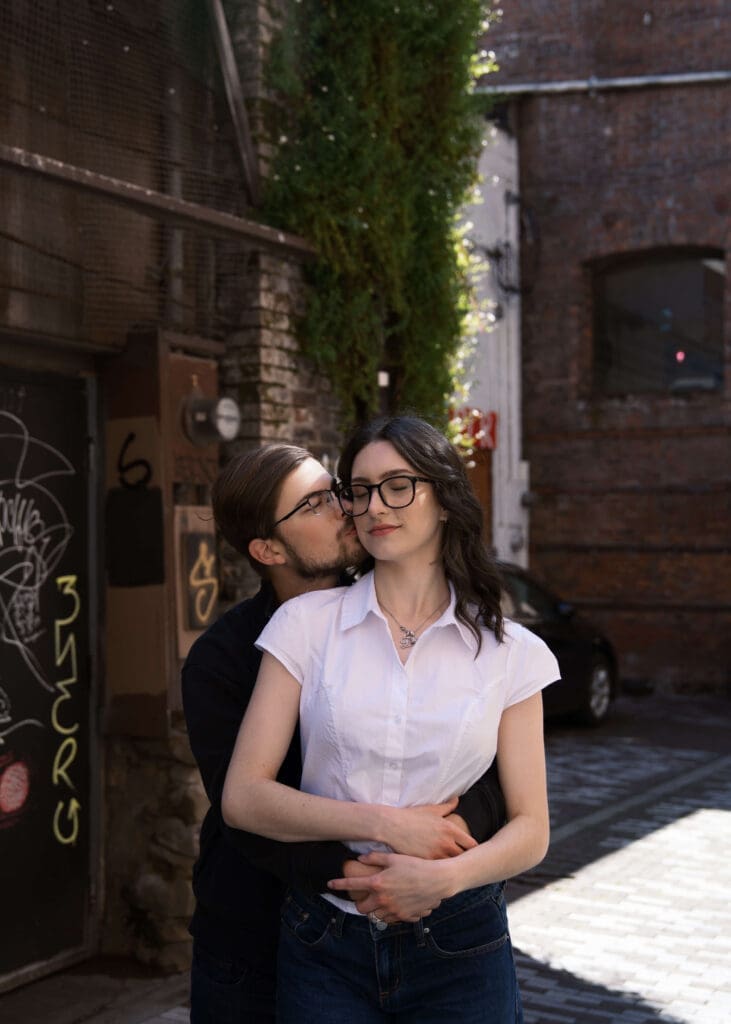 man kissing wife on the cheek in alley of pioneer sqaure for engagement