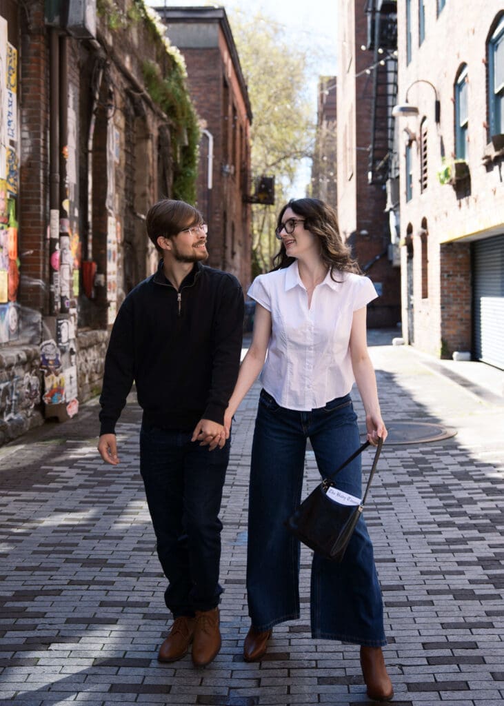couple holding hands and walking in alley for pioneer square engagement photos