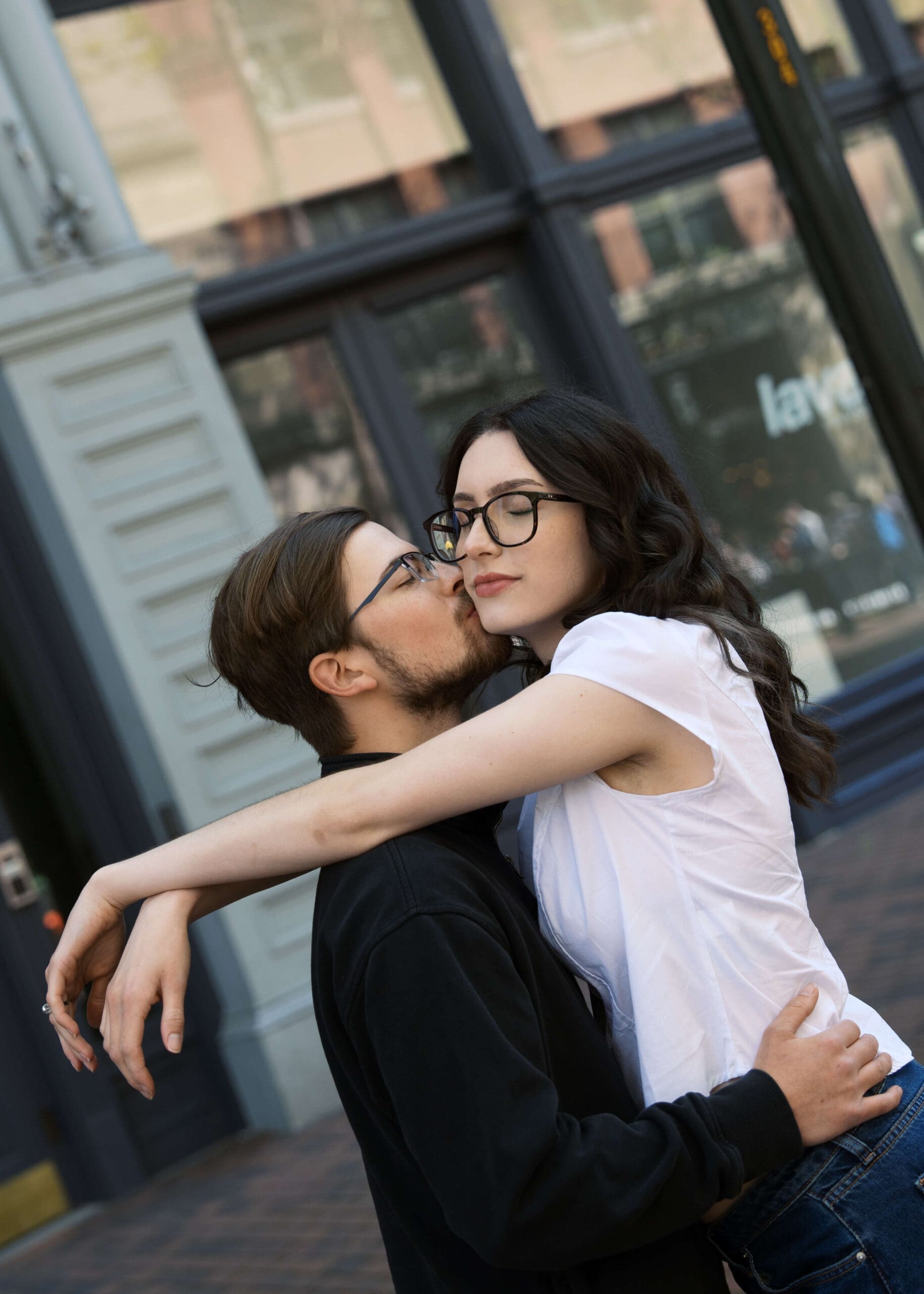 man kissing wife with glasses on the cheek at Pioneer sqaure engagement