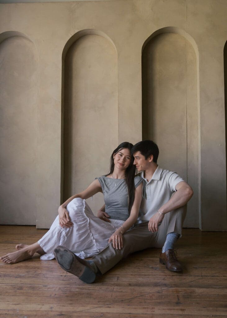 couple sitting down in a Seattle photo studio leaning against each other wearing white and grey 