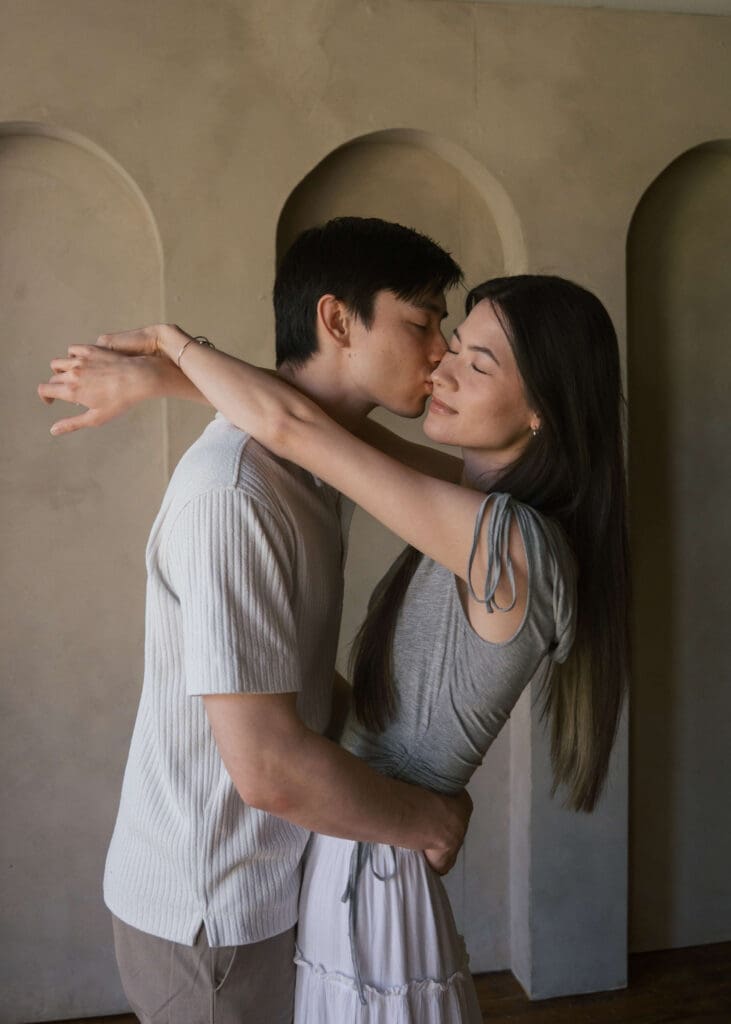 man kissing his partner on the cheek while she has her arms around his neck 