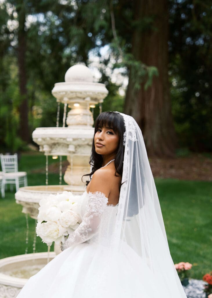 bride looking over her shoulder with fountain in the background outside wedding venue in Washington