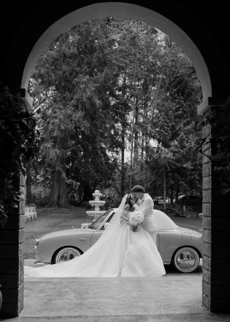 couple kissing in arch in front of vintage car at Hidden Stone Palace