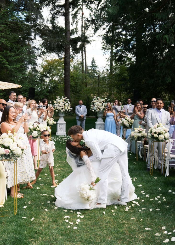 aisle dip and kiss after outdoor ceremony while guests throw flower petals