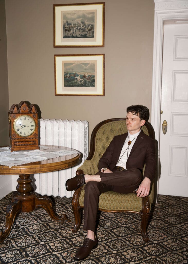 groom in a brown suit sitting in a chair posing for portraits