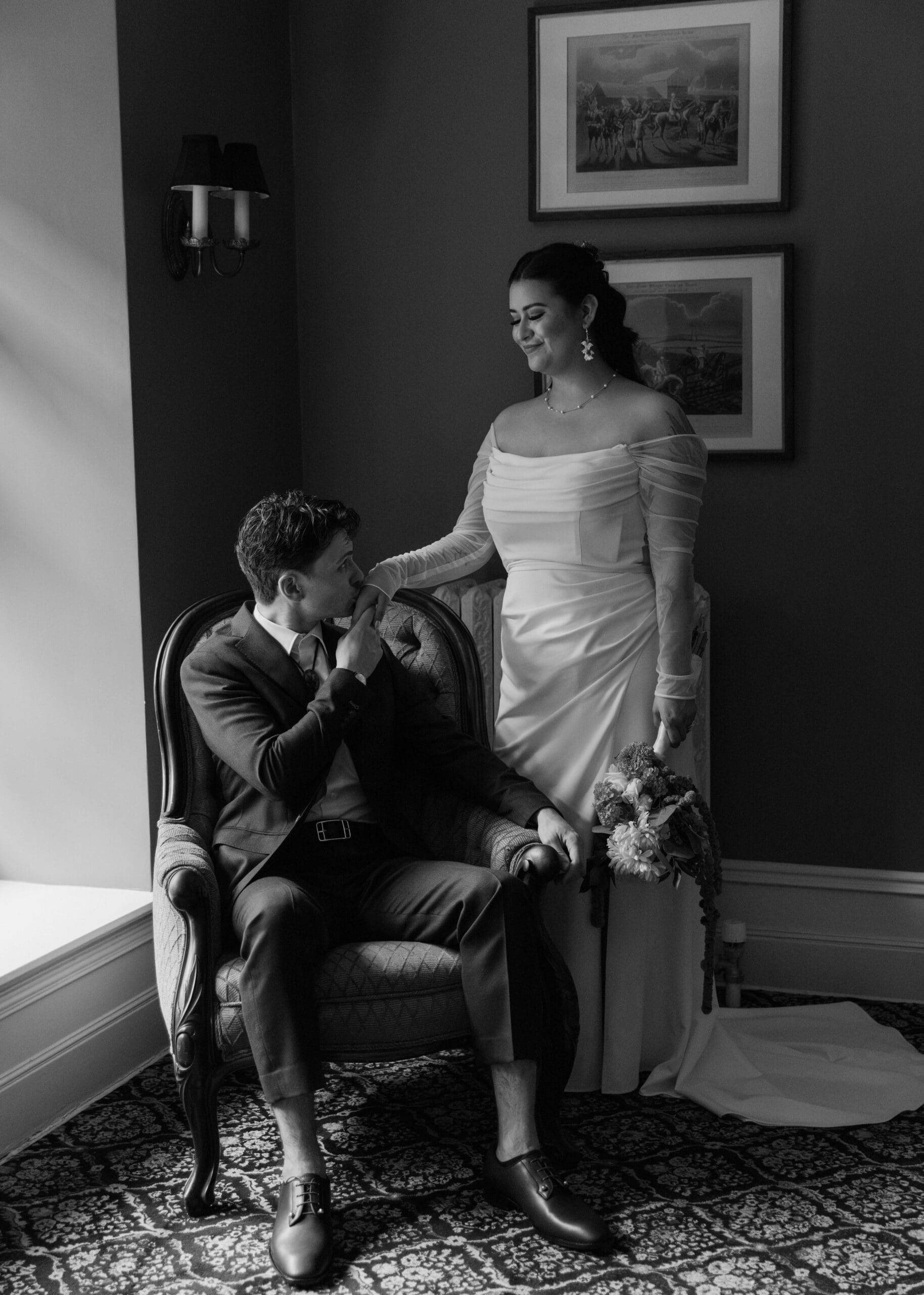 groom kissing his bride's hand while sitting in a chair at Stimson-Green Mansion