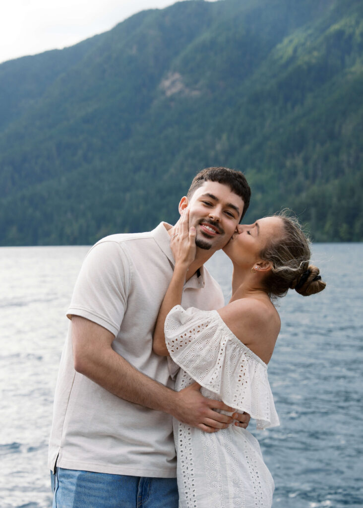 woman kissing her fiance on the cheek at the lake 