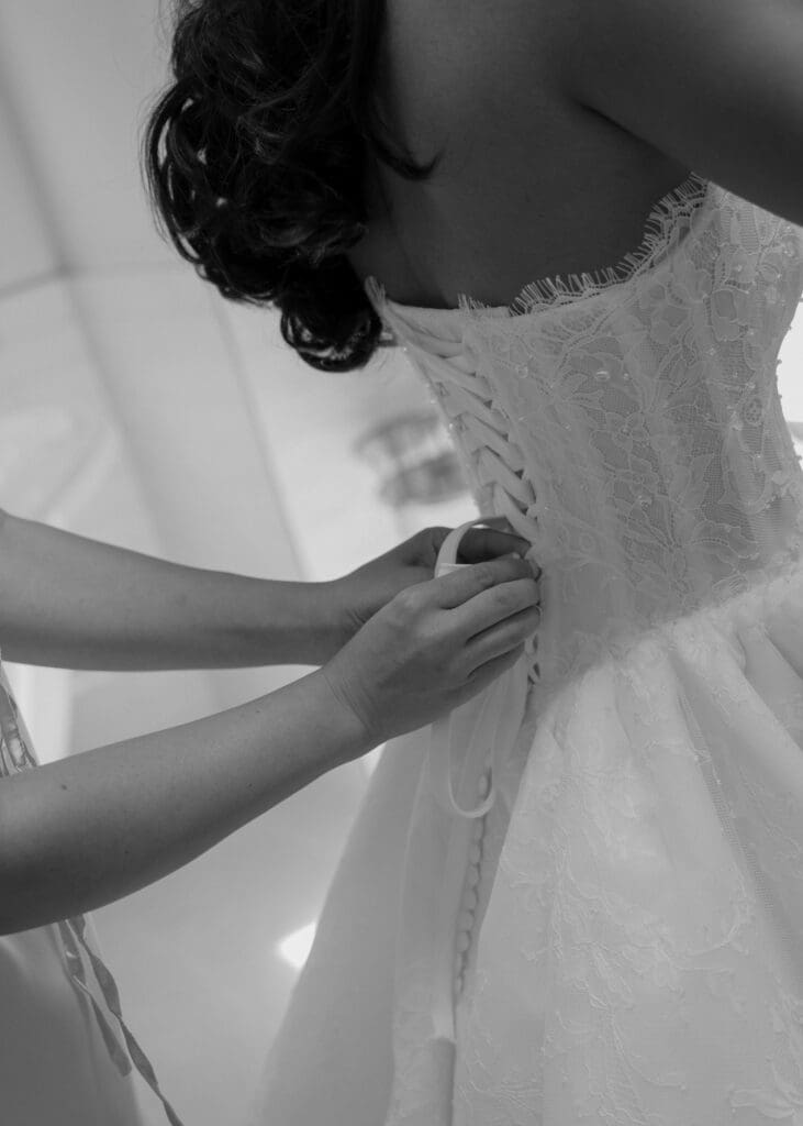 bridesmaid buttoning up the bride's dress on her wedding day at theBindery