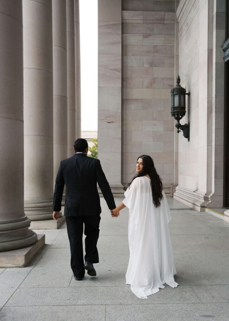 bride looking over her shoulder while walking and holding her husband's hand 