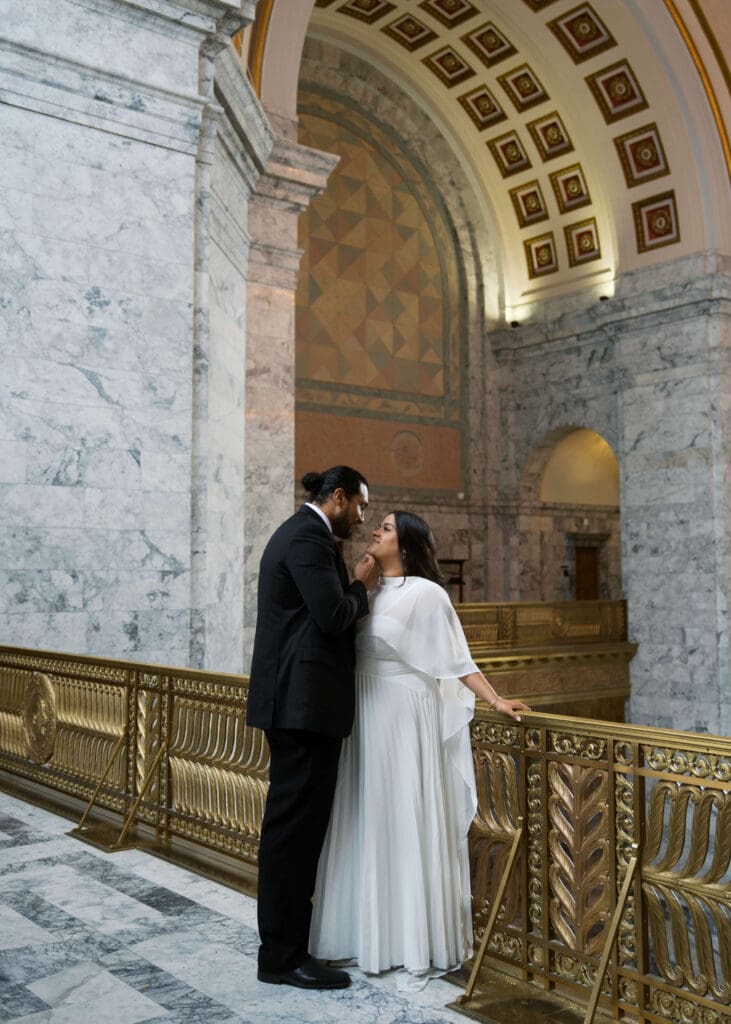 bride leaning on the rail while groom cups her face at Washington state capitol wedding